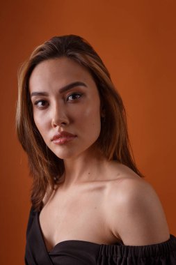 Turuncu arka planda koyu yakalı siyah elbise giyen zarif bir manken.