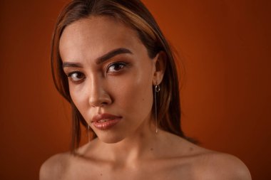 Akşam makyajlı, çıplak omuzlu, küpeli güzel Asyalı kız kameraya bakıyor.