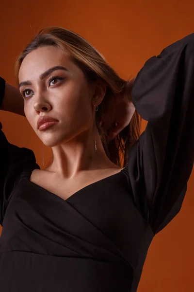 Modelo elegante vestindo vestido preto com decote profundo posando no fundo laranja — Fotografia de Stock