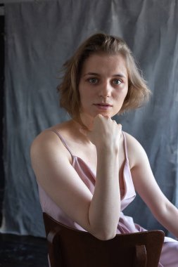 Kısa saçlı, pembe takım elbiseli, stüdyoda sandalyede oturan beyaz bir kadın.