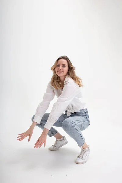 Young cute smiling caucasian girl posing in white shirt, blue jeans at studio — Stock Photo, Image