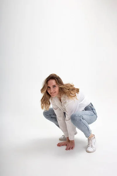 Joven linda sonriente chica caucásica posando en camisa blanca, pantalones vaqueros azules en el estudio — Foto de Stock