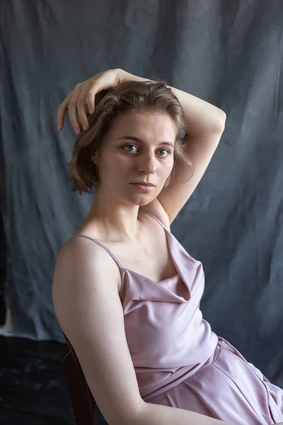 Kaukasiska ung kvinna med kort hår i rosa kostym sitter på stol i studio — Stockfoto