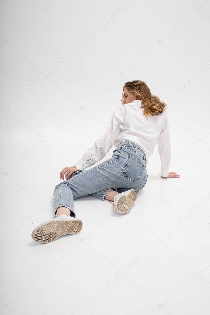 caucasian woman posing in shirt and blue jeans, sitting on white studio floor