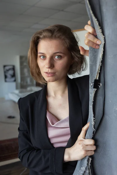 caucasian woman with short hair posing in black suit jacket, holding curtain