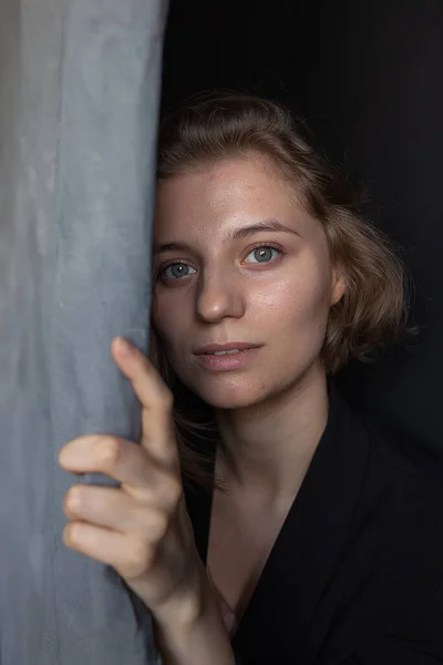 Caucasian woman with short hair posing in black suit jacket, holding curtain — Stock Photo, Image