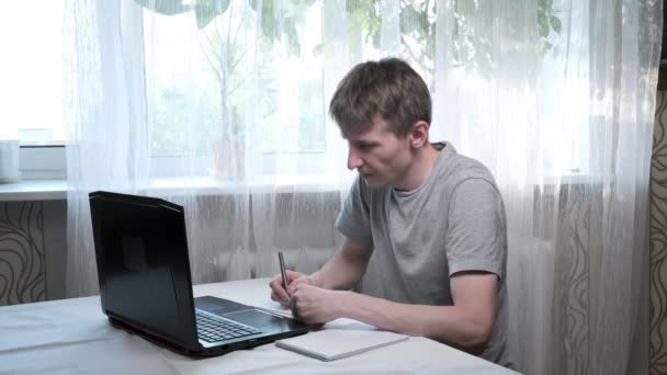 Young man talks to tutor, writes notes. online education at laptop, remote job — Stock Video