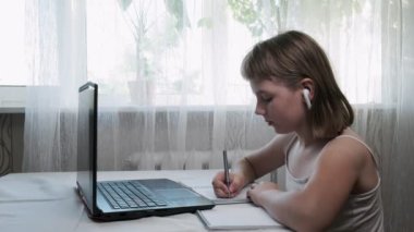 Kulaklıklı küçük bir kız, evde bilgisayar aracılığıyla internet öğretmeniyle çalışıyor.