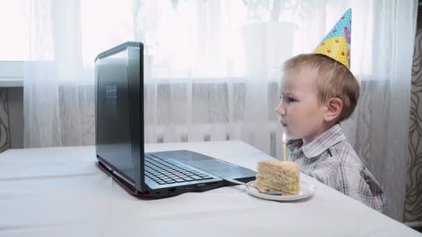 Junge sitzt am Tisch mit Laptop und Stück Geburtstagstorte mit brennender Kerze — Stockvideo