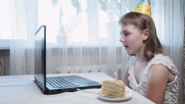Κορίτσι κάθεται στο τραπέζι με φορητό υπολογιστή, φυσά αναμμένο κερί στην τούρτα γενεθλίων — Αρχείο Βίντεο