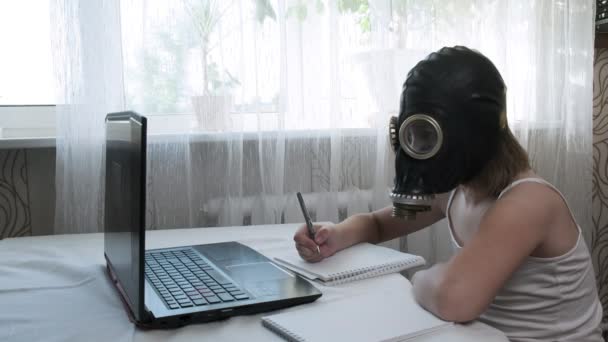 Little girl wears gas mask, does homework with laptop, writes notes in notebook — Stock Video