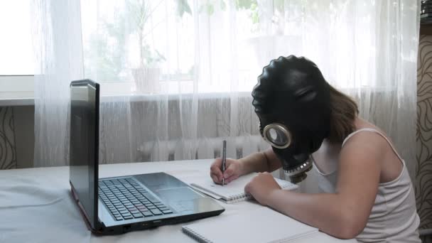 Klein meisje in gas masker doet huiswerk met laptop, schrijft notities in notebook — Stockvideo