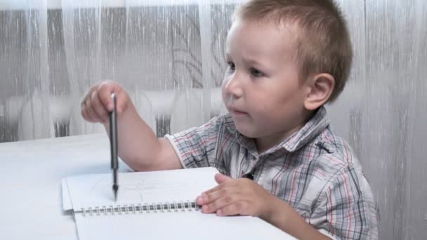 Klein Kaukasisch jongen tekent krabbels en krabbels furieus in notebook aan tafel — Stockvideo