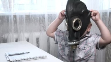 Kısa saçlı beyaz çocuk gaz maskesi takmaya çalışıyor, babası ona yardım ediyor.