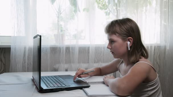 Little girl in headphones, studies at home with internet teacher via laptop — Stock Video