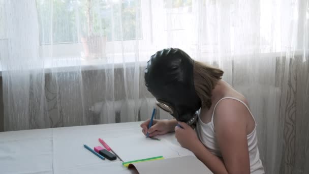 Menina em máscara de gás senta-se à mesa, desenha ilustração com canetas de feltro no álbum — Vídeo de Stock