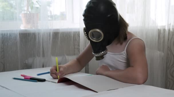 Girl in gas mask sits at table, draws illustration with felt pens in album — Stock Video