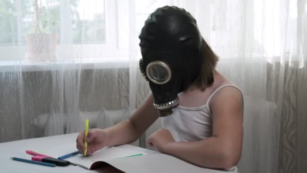 Girl in gas mask sits at table, draws illustration with felt pens in album — Stock Video