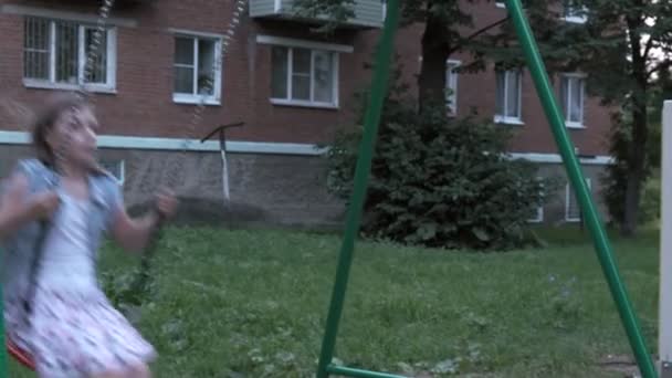 Lille kaukasisk pige svingende på swing med kæder på værftet, ser på kameraet – Stock-video