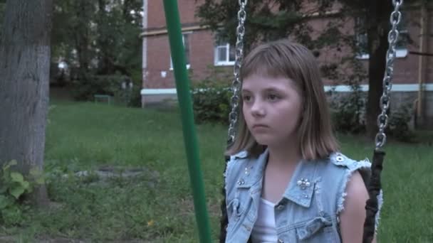Smutna mały biały dziewczyna huśtawka na huśtawka na podwórku, patrząc w aparat — Wideo stockowe