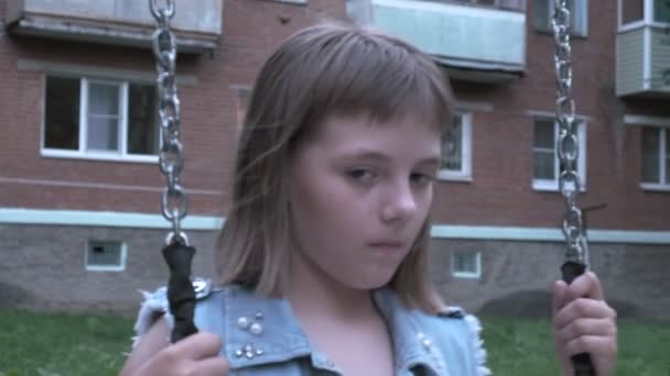 Trist eftertænksom lille kaukasisk pige svinger på swing på værftet, ser på kameraet – Stock-video