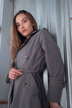 Gri trençkotlu çekici Asyalı model dışarıda duvarın yanında duruyor.