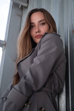 Gri trençkotlu çekici Asyalı model dışarıda duvarın yanında duruyor.