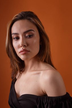 Turuncu arka planda siyah elbise giyen zarif Asyalı genç manken.