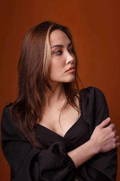 Elegantes Model in schwarzem Kleid mit tiefem Ausschnitt posiert auf orangefarbenem Hintergrund — Stockfoto