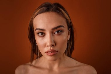 Akşam makyajlı, çıplak omuzlu, küpeli güzel Asyalı kız kameraya bakıyor.