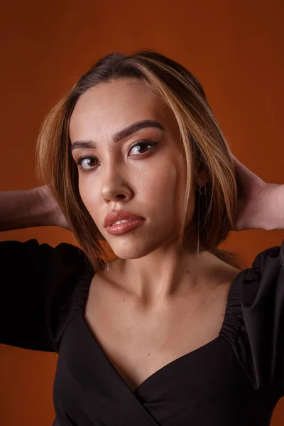 Elegante modelo con vestido negro con escote profundo posando sobre fondo naranja —  Fotos de Stock