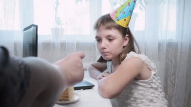 Kız dizüstü bilgisayarla ve yanan mumla doğum günü pastasıyla masada oturuyor.