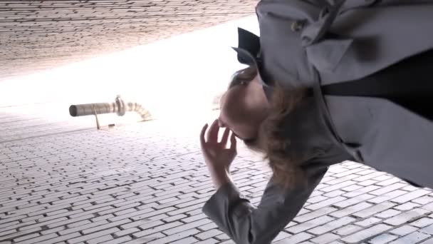 Азиатская красивая модель в плаще, стоящая возле стен, снятая из нижней точки — стоковое видео
