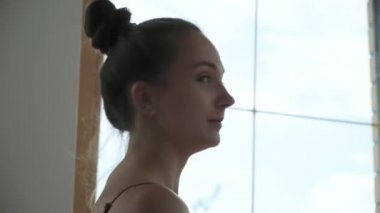 Güzel esmer kadın, saçları toplanmış pencerenin önünde duruyor, gülümsüyor ve gülüyor.