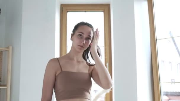 Sportig brunett söt kvinna i sportkläder står vid fönstret, fixar hår — Stockvideo