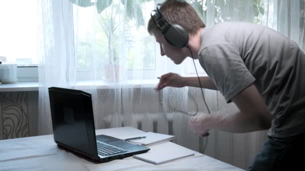 Focused young caucasian man sits down at table, connects headphones to laptop — Stock Video