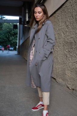 Gri trençkotlu çekici Asyalı model dışarıda duvarın yanında duruyor.