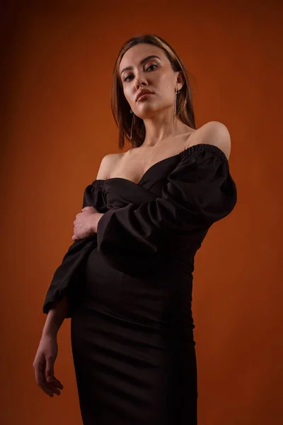 Elegant model in zwarte jurk met diepe halslijn poserend op oranje achtergrond — Stockfoto