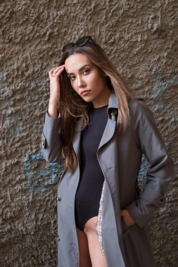 Gri trençkotlu ve açık havada siyah takım elbiseli çekici Asyalı genç bir model.