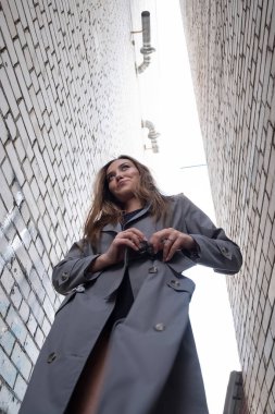 Trençkotlu çekici Asyalı model alt noktadan çekilen duvarların yanında duruyor.