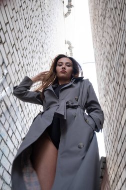 Trençkotlu çekici Asyalı model alt noktadan çekilen duvarların yanında duruyor.