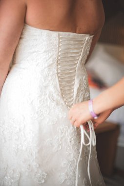 Gelin yardım alarak giyiniyor, kadın geri dönüyor. 