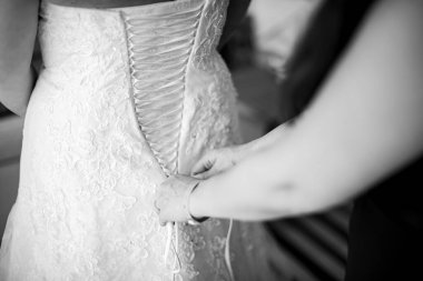 Siyah beyaz fotoğraf, gelin yardım alarak giyiniyor.