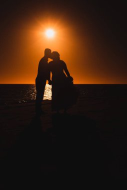 Gün batımına karşı aşık çiftler öpüşüyor. 