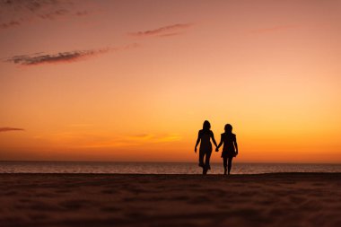 Çiftler gün batımına karşı el ele tutuşup kumsalda yürüyorlar. 