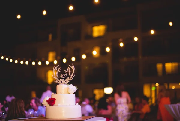 wedding cake on table, blurred bokeh lights on background and people dancing at party