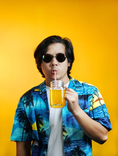 亚洲男子喝橙汁戴墨镜反对黄色背景 — 图库照片