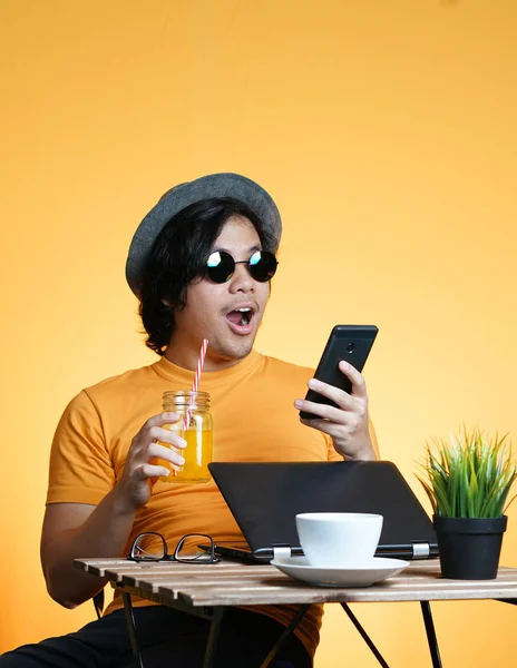 年轻男子震惊和兴奋持有智能手机 而在夏季假期工作对黄色背景 — 图库照片