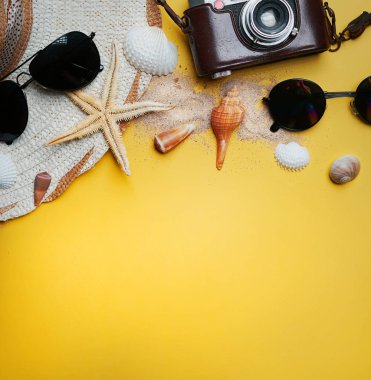 Yaz plaj aksesuarları sarı zemin üzerine. Kamera, deniz yıldızı, güneş gözlüğü, deniz kabuğu ve şapka. Metin için düz yatıyordu yer