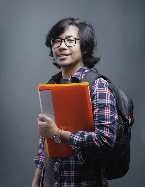 亚洲大学生的肖像在拿着灰色背景的书时微笑在相机上 — 图库照片